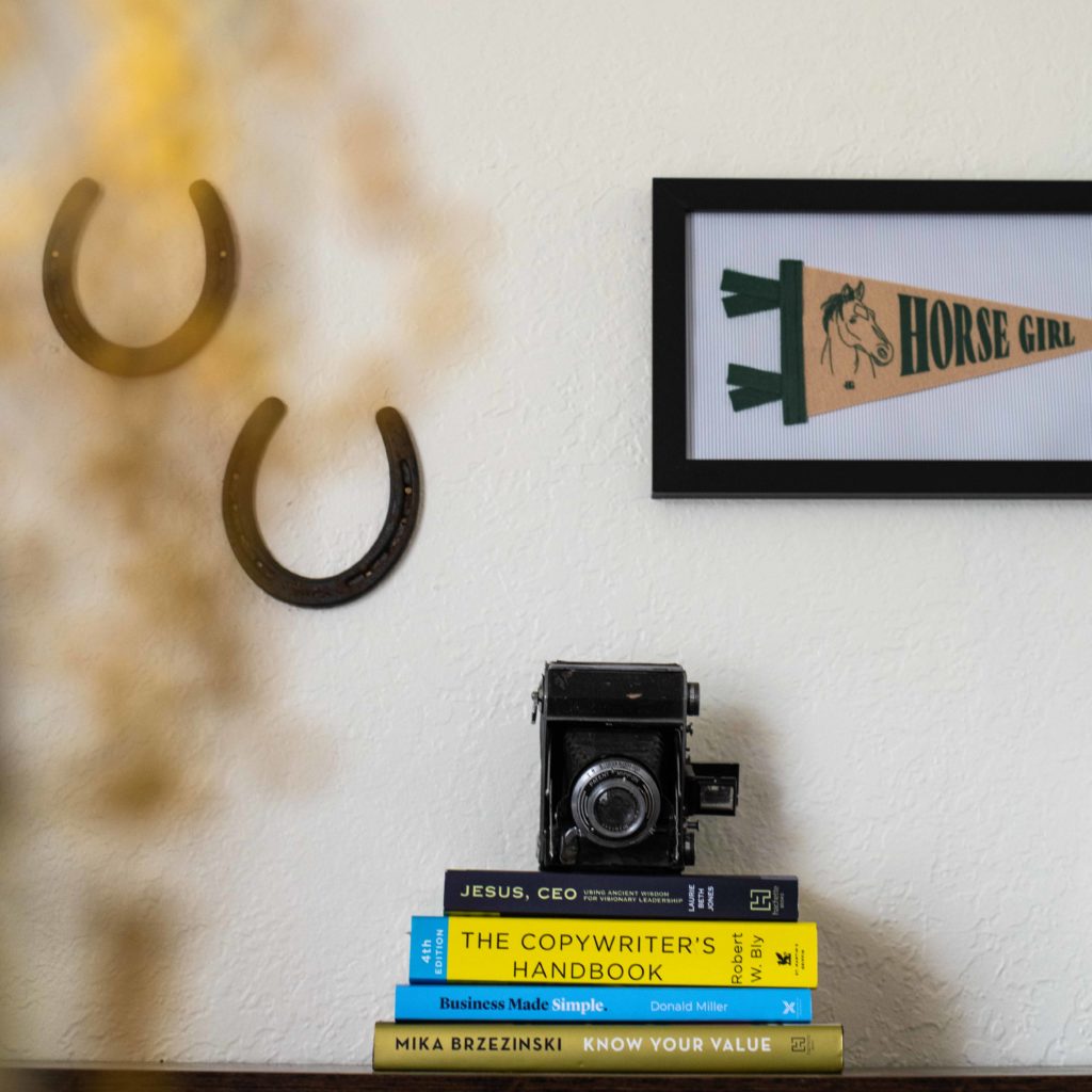 a stack of entrepreneurship books with an antique camera and horse shoes along with a framed horse girl banner