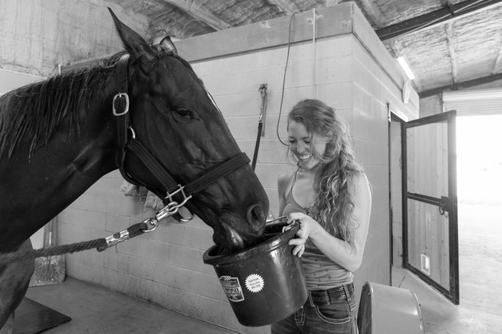 A girl holds a bucket of Gatorade in a bucket up toward her horse