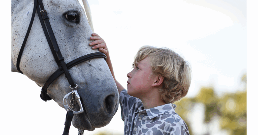 Candid photograph of a young rider embracing and looking up at his horse